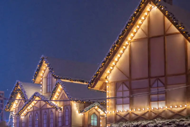 Warm white Christmas lights tracing the edges of several steep gables at dusk